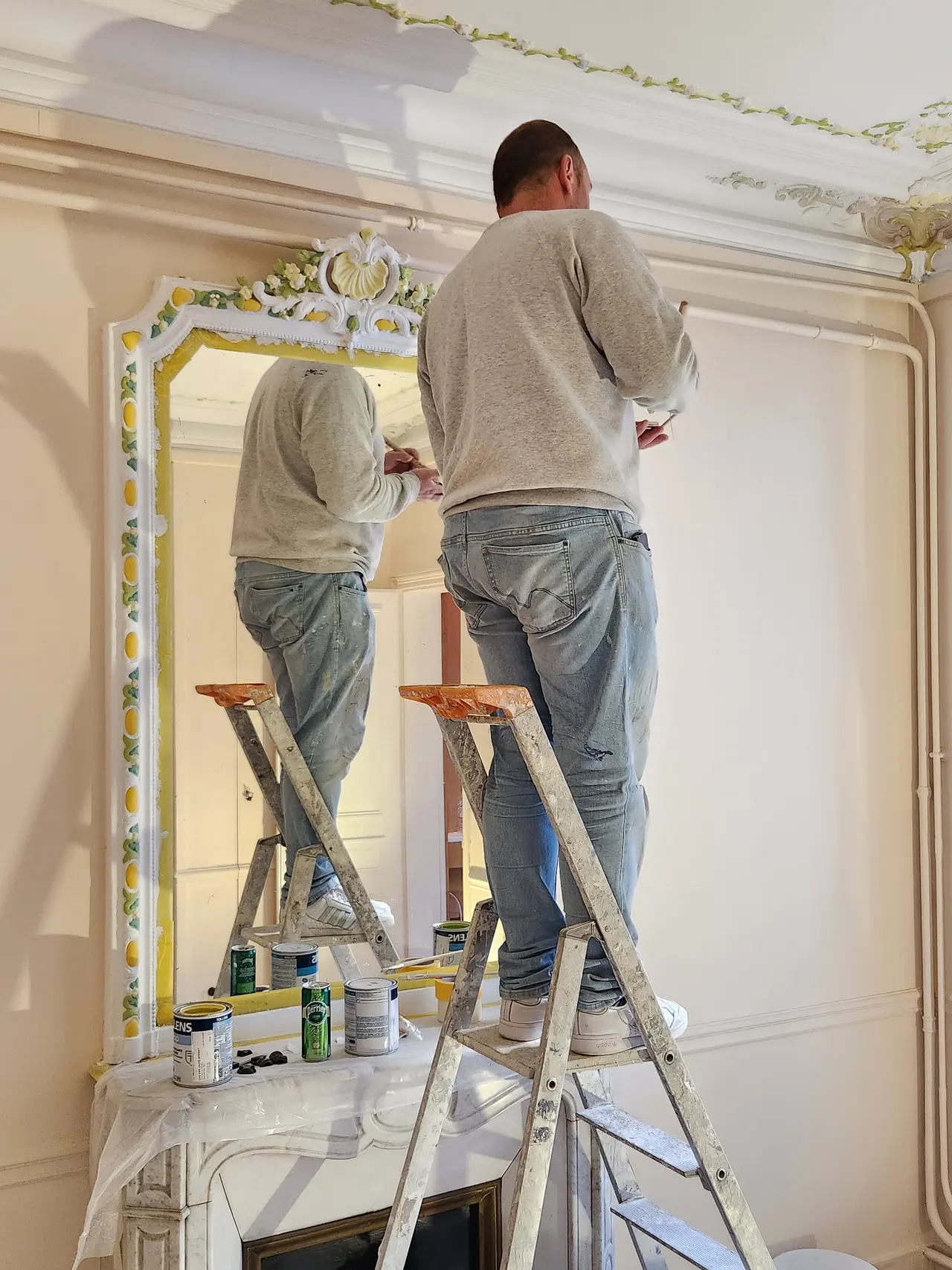 Un peintre reprend un décor floral au-dessus d'un miroir.