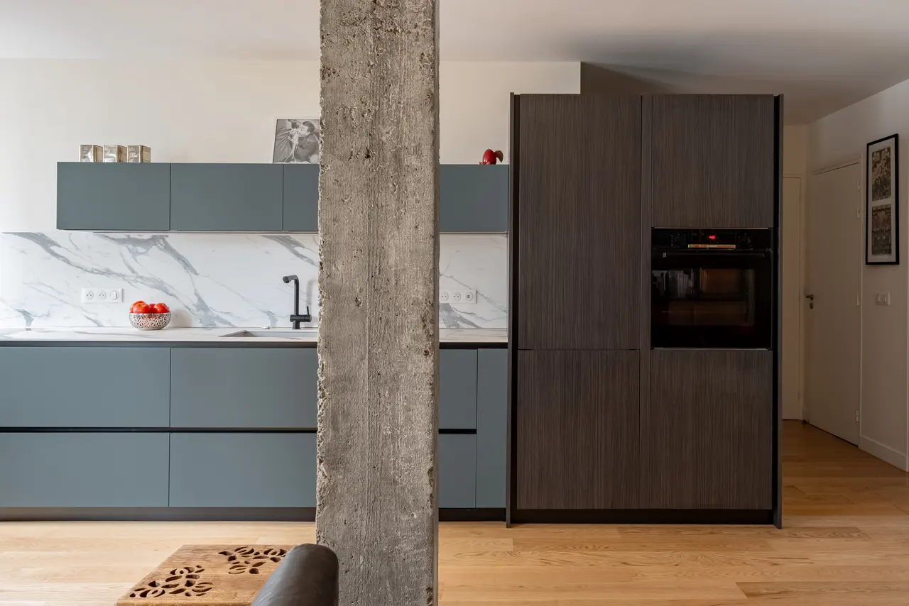Cuisine linéaire gris ardoise derrière un poteau en béton brut.