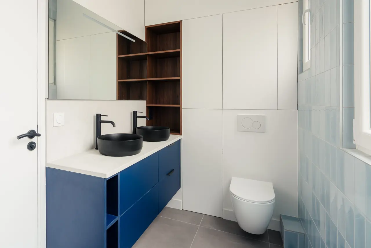 Salle de bains : double vasque noire sur meuble bleu.