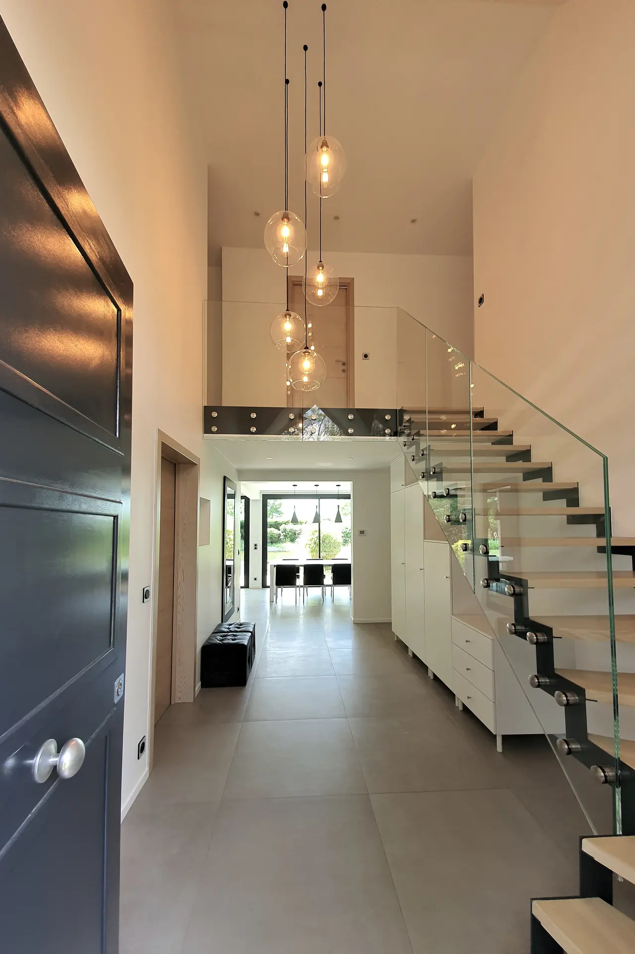 Entrée de maison : escalier à limon central, garde-corps en verre, rangements sous les marches.