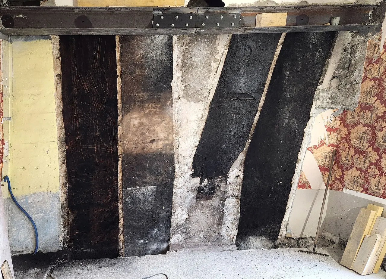 Pans de bois anciens posés en diagonale, sous une poutre neuve boulonnée.