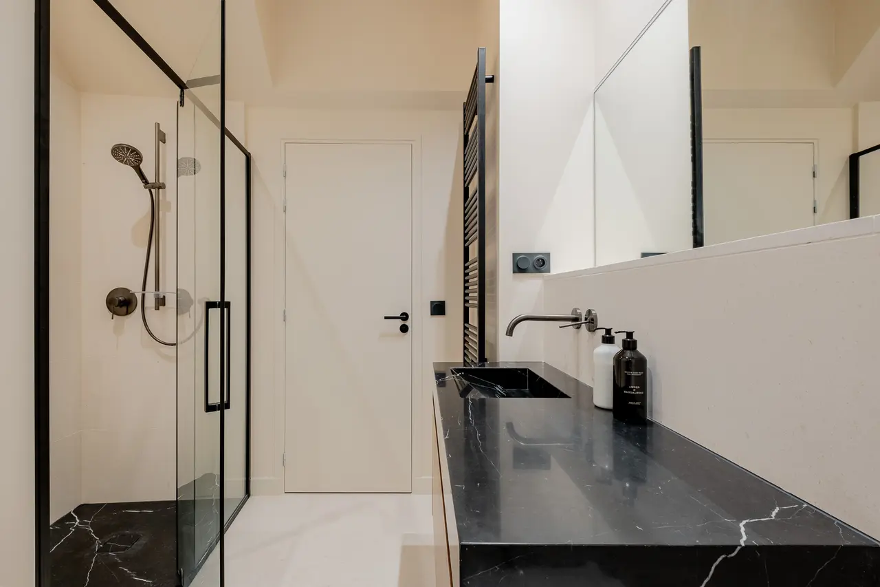 Salle de bains : douche vitrée, vasque sur plan en pierre noire, meuble en noyer.